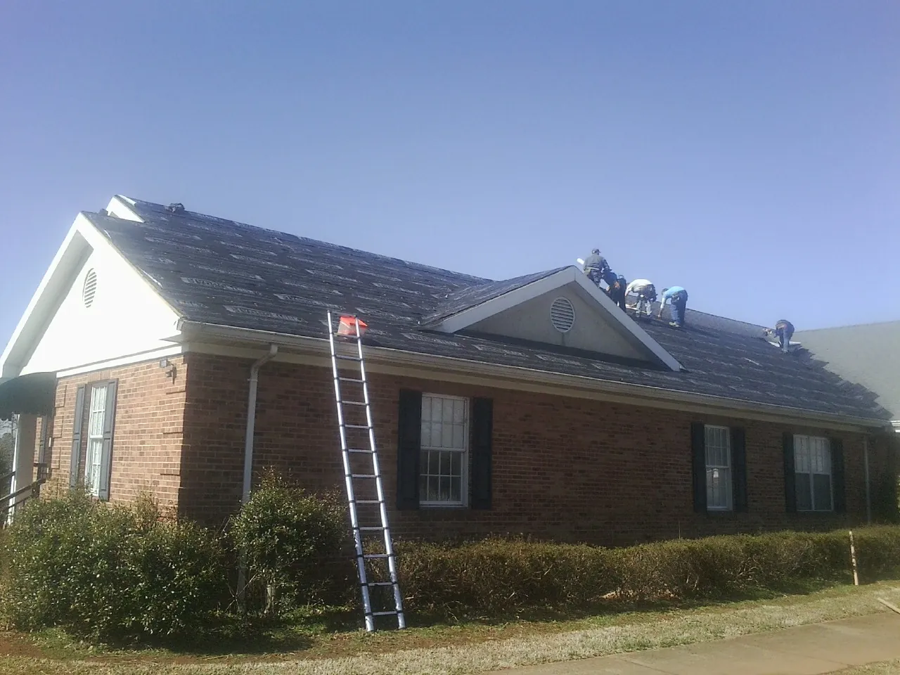 Crew tearing shingles off a brick ranch roof with a ladder set — Metal Roof Repair work by our crew in Huntsville