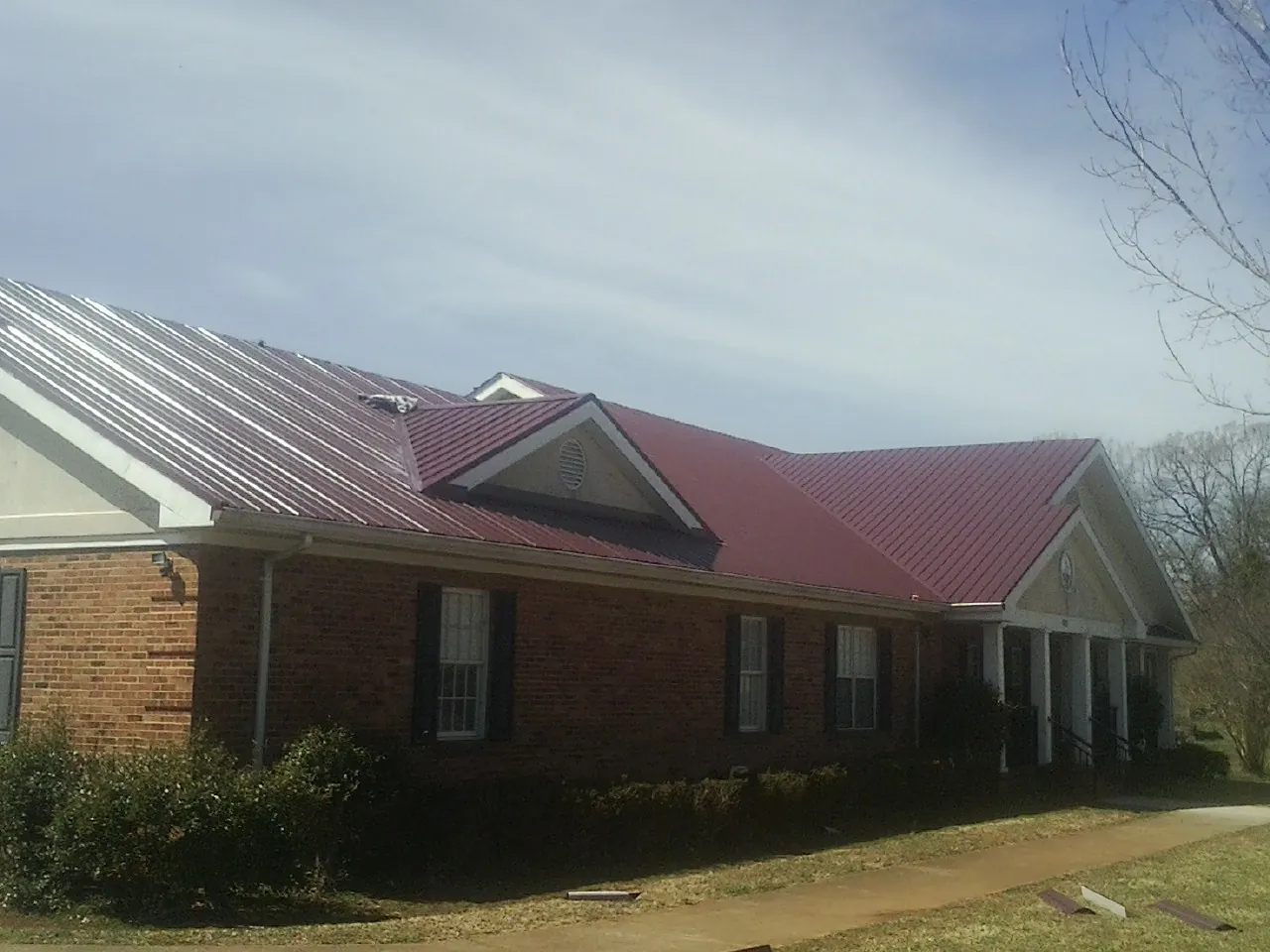 Red metal roof with gabled entries on a long brick building, from a Hail Damage Roof Repair job in Huntsville