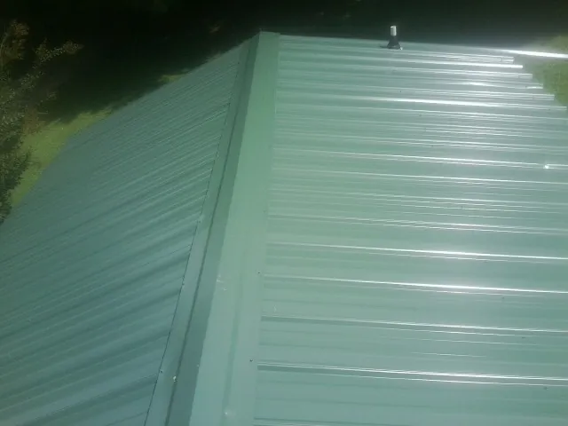 New green metal panels meeting at the ridge of a roof — Flat Roof Repair work by our crew in Huntsville