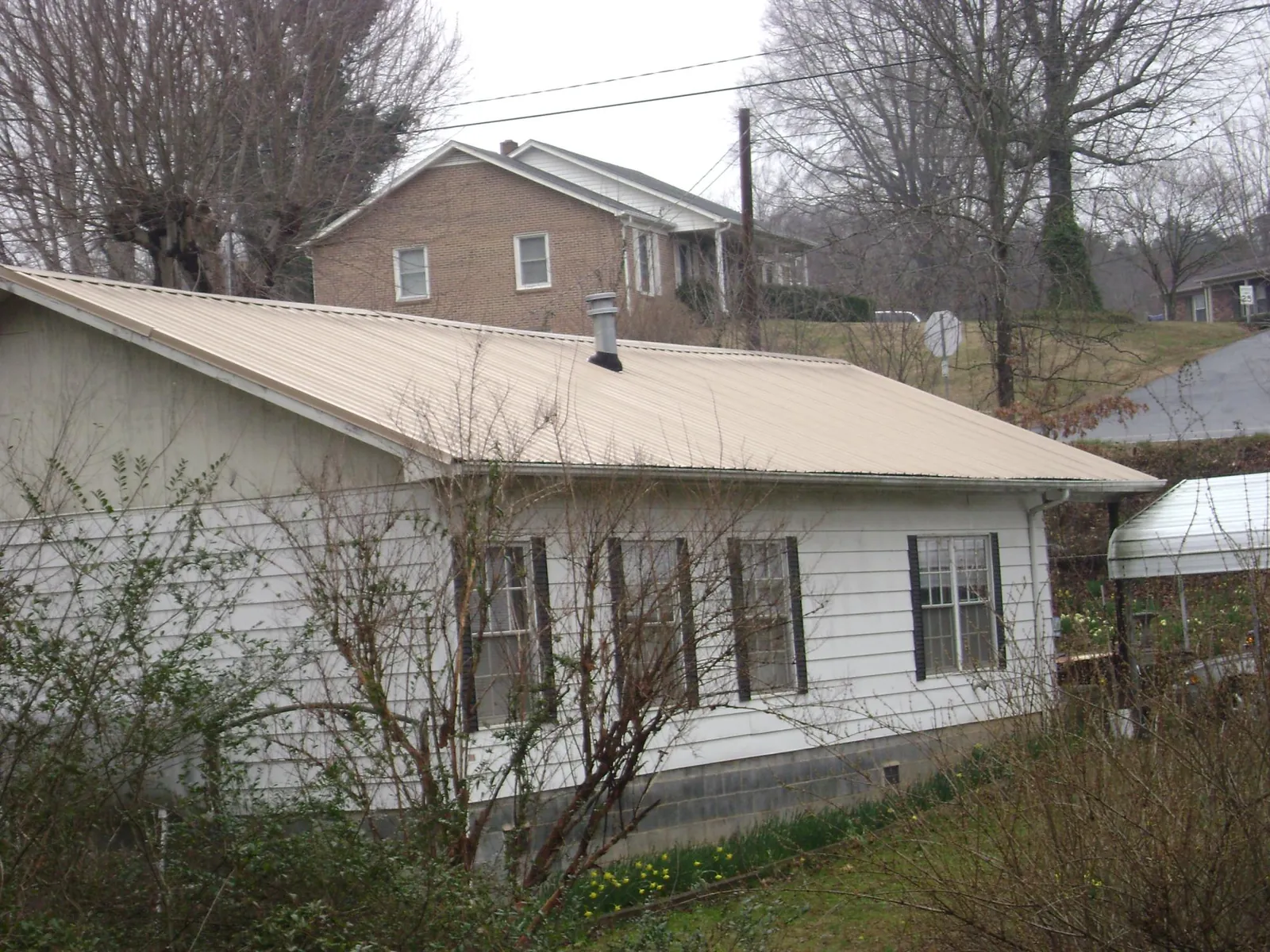 Tan metal roof on a white sided house set into a hillside — Commercial Roofing by Roofing Brothers in Huntsville